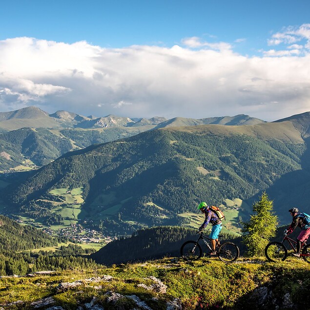 Two mountain bikers riding on a mountain with a view of Bad Kleinkirchheim – active holiday at hiking hotel Eschenhof in the Nockberge
