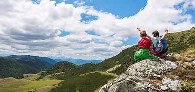 Zwei Kinder sitzen auf einem Felsen mit Panorama über die Nockberge bei Bad Kleinkirchheim in Kärnten