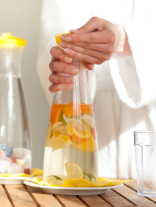 Persona in accappatoio apre una caraffa con acqua e agrumi freschi nell’area wellness del Naturhotel Eschenhof a Bad Kleinkirchheim